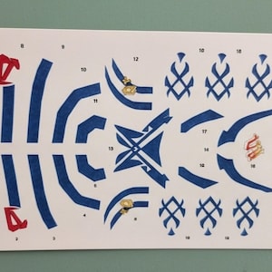 May include: A sheet of paper with various blue and red shapes, including curved lines, geometric designs, and decorative elements. Some shapes have gold accents. The elements are numbered.