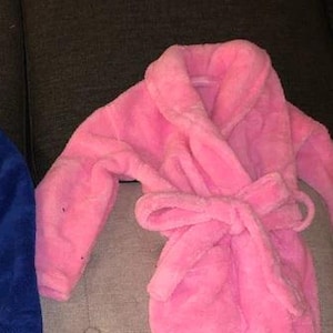 May include: Two plush bathrobes, one blue and one pink, with a tie belt. The robes are made of soft, fluffy material.