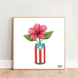 Puede incluir: Impresión enmarcada de una vibrante flor de hibisco roja con hojas verdes, que emerge de una lata decorada con la bandera de Puerto Rico. La obra de arte está sobre un fondo blanco, con la firma del artista en la esquina inferior derecha.