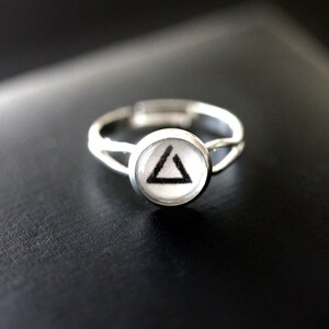 Op de afbeelding: Een zilveren ring met een witte cabochon met een zwart driehoekontwerp.