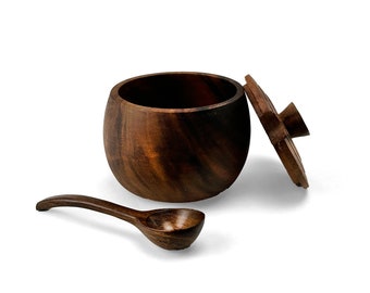 May include: A dark brown wooden salt cellar with a lid and a matching wooden spoon. The salt cellar is round and has a smooth, polished finish.