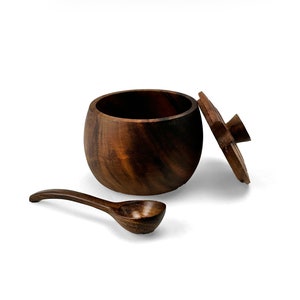 May include: A dark brown wooden salt cellar with a lid and a matching wooden spoon. The salt cellar is round and has a smooth, polished finish.