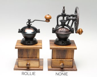 Peut inclure: Deux moulins à café anciens avec des corps en métal foncé et des bases en bois. L'un a une manivelle, l'autre une grande roue. Les bases en bois ont des tiroirs avec des boutons ronds. Le mot "ROLLIE" est imprimé sous un moulin, et "NONIE" sous l'autre.