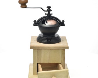 May include: A black cast iron coffee grinder with a wooden base and a drawer. The grinder has a wooden handle and a crank.