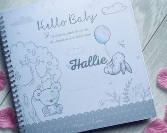 Puede incluir: Un libro de recuerdos para bebés gris y blanco con encuadernación en espiral. La portada presenta una linda ilustración de un conejito sosteniendo un globo, un osito de peluche y el texto "Hello Baby" y "Hallie". El libro también incluye el texto "Inserte la foto del bebé aquí" y "Hecho con amor".