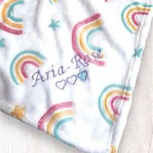 May include: White plush blanket with a rainbow pattern and stars. The blanket is personalized with the name "Aria-Rose" and three hearts.