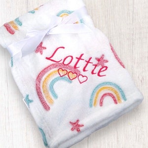 May include: White fleece baby blanket with a rainbow and star pattern. The blanket is personalized with the name "Lottie" in pink embroidery.