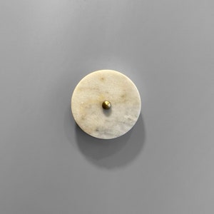 May include: A round, white marble coaster with a gold knob in the center.