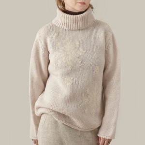 Può includere: Un maglione color crema a collo alto con un discreto motivo a fiocco di neve. Il maglione è lavorato a maglia e ha una vestibilità rilassata.