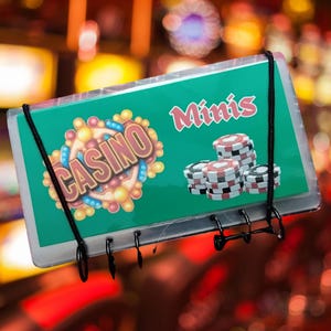 May include: A green sign with the word "Casino" in a decorative font and the word "Minis" in red. Stacks of casino chips are visible. The sign is held by a black metal frame with a black elastic cord.