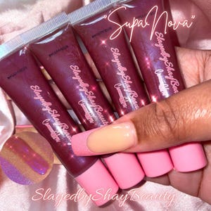 May include: Four tubes of clear lip gloss with a pink iridescent shimmer. The tubes are labeled "Slayedby Shay Beauty" and "Supa Nova".