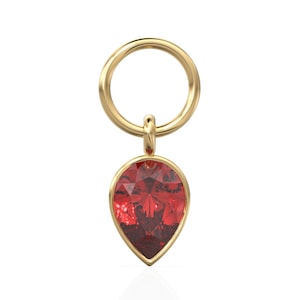 Könnte beinhalten: Ein goldfarbener Anhänger mit einem tropfenförmigen, facettierten, roten Edelstein. Der Anhänger hängt an einer kreisförmigen Schlaufe. Der Edelstein ist etwa 2 cm lang und 1,3 cm breit.