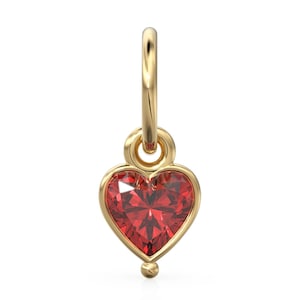 Könnte beinhalten: Goldener Anhänger mit einem roten herzförmigen Edelstein. Der Anhänger hat eine Öse oben zum Anbringen an einem Armband oder einer Halskette.