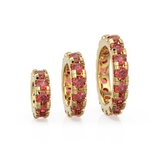 May include: Three gold rings with red gemstones. The rings are different sizes, with the largest ring in the back and the smallest ring in the front.