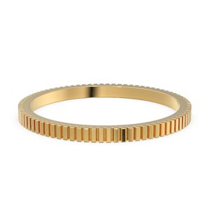 May include: A gold-colored ring with a unique design. The ring features a series of vertical rectangular bars around the entire band. The ring is set against a white background, highlighting its intricate details and metallic sheen.