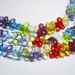 May include: A rainbow of faceted gemstone beads in a flower shape. The beads are strung on a wire and are arranged in a rainbow pattern. The beads are made of various gemstones, including amethyst, aquamarine, citrine, peridot, ruby, and sapphire.