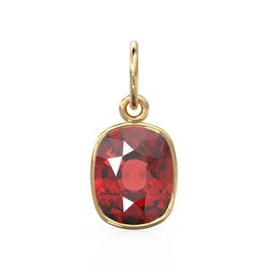 May include: A gold pendant with a cushion-cut, deep red gemstone. The gemstone is set in a gold bezel and has a faceted surface. The pendant has a small gold loop at the top for attaching to a chain. The gemstone is a deep red colour.