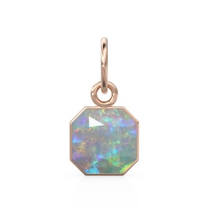 May include: A rose gold pendant with an octagonal opal gemstone. The opal displays a play of color with iridescent hues of blue, green, and yellow. The pendant has a small loop for attaching to a chain or bracelet.
