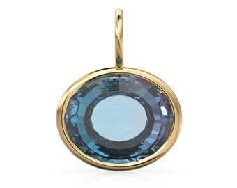 May include: A round pendant with a gold-colored bezel and bail. The pendant features a large, faceted, blue-green gemstone. The gemstone has a central, lighter blue circle. The pendant is designed to be worn as jewelry.