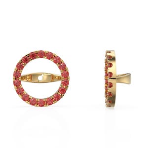 May include: A pair of gold-colored earrings. Each earring features a circular design encrusted with small, red gemstones. The earrings have a post-and-clasp closure. One earring is shown from the side, displaying the thickness and construction.