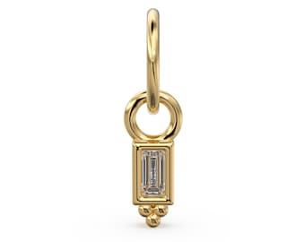 Puede incluir: Encanto de oro con un pequeño diamante rectangular y un detalle de cuentas. El encanto está unido a un aro de oro.