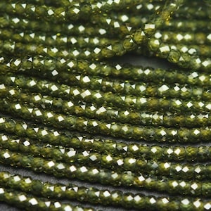 Peut inclure: Un brin de perles facettées vert foncé. Les perles sont petites et rondes, et elles sont enfilées sur un fil transparent.