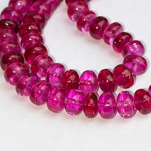 May include: A strand of pink gemstone beads. The beads are round and have a slightly faceted appearance. The beads are strung on a thin cord.