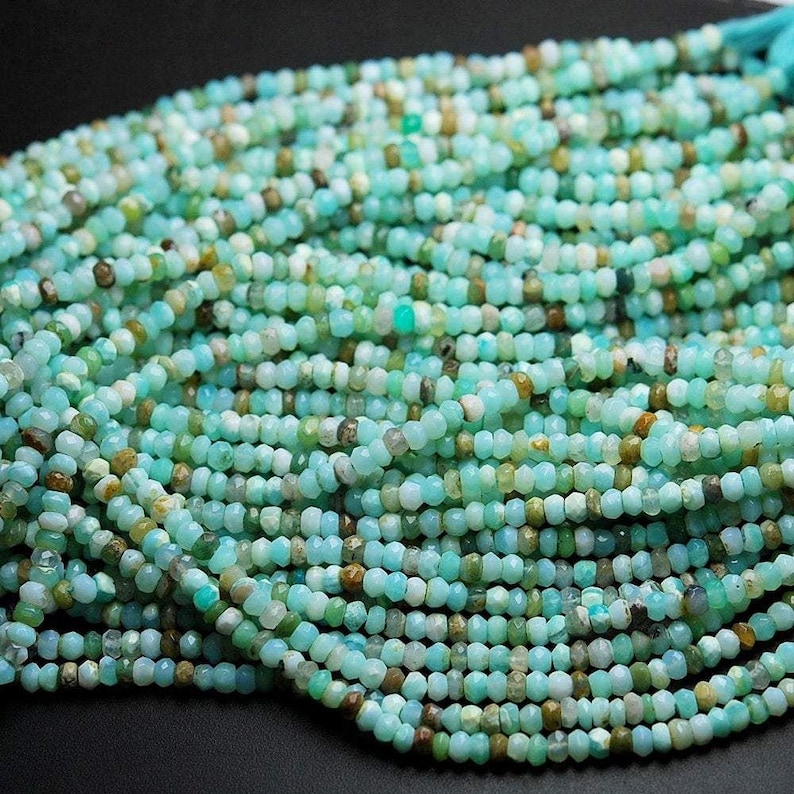 May include: A strand of light blue, green, and brown opal beads. The beads are faceted and have a slightly irregular shape. The beads are strung on a clear thread.
