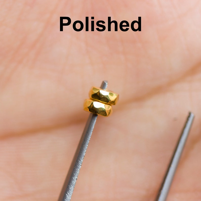 May include: Two gold-colored metal rings stacked on top of each other. The rings are polished and have a faceted design. The rings are held by a pair of tweezers.