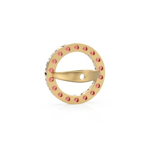 May include: A gold ring with a circular design. Small pink gemstones are set around the outer edge. A curved bar spans the centre, with a small hole. The ring is set against a white background.