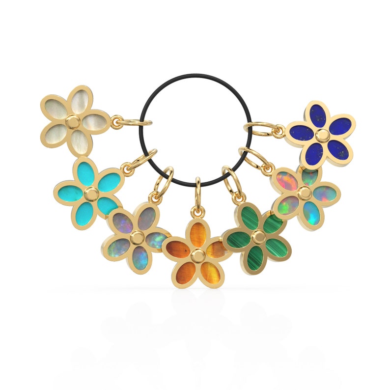 May include: A set of seven gold flower charms with different colored gemstones. The charms are attached to a black elastic band.