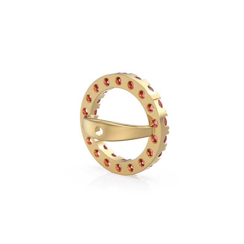 May include: A gold ring with a circular design, featuring small, orange gemstones set around the outer edge. The ring has a unique, open design with a curved band for the finger. The gemstones are evenly spaced, creating a sparkling effect.