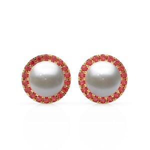 May include: A pair of stud earrings with a large, round, white pearl centre, encircled by a halo of small, red gemstones. The setting is gold-coloured, contrasting with the white and red elements.