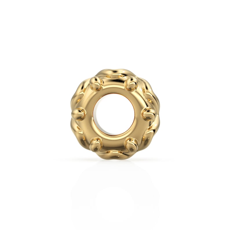 May include: A gold-colored charm with a textured, circular design. The charm has a small hole in the center.