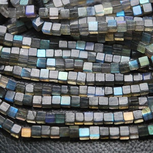 May include: A strand of dark gray square-shaped labradorite beads with iridescent blue and green flashes.