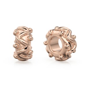 May include: Two rose gold charm beads with a wavy, textured design and small round accents.