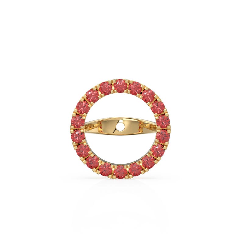 May include: A gold ring featuring a circular design, embellished with small, round, red gemstones. The ring has a band across the centre. The ring is set against a white background. The gemstones are a vibrant red colour, adding a touch of elegance.