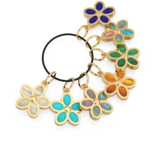 May include: A set of seven gold flower charms with different colored gemstones. The charms are attached to a black elastic cord.