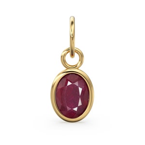May include: A gold pendant with an oval-cut ruby gemstone. The ruby is a deep red color and is set in a gold bezel. The pendant has a small loop at the top for attaching to a chain. The overall design is simple and elegant.