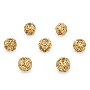 May include: Six gold-colored metal beads with a floral design. The beads are round and have a hollow center.