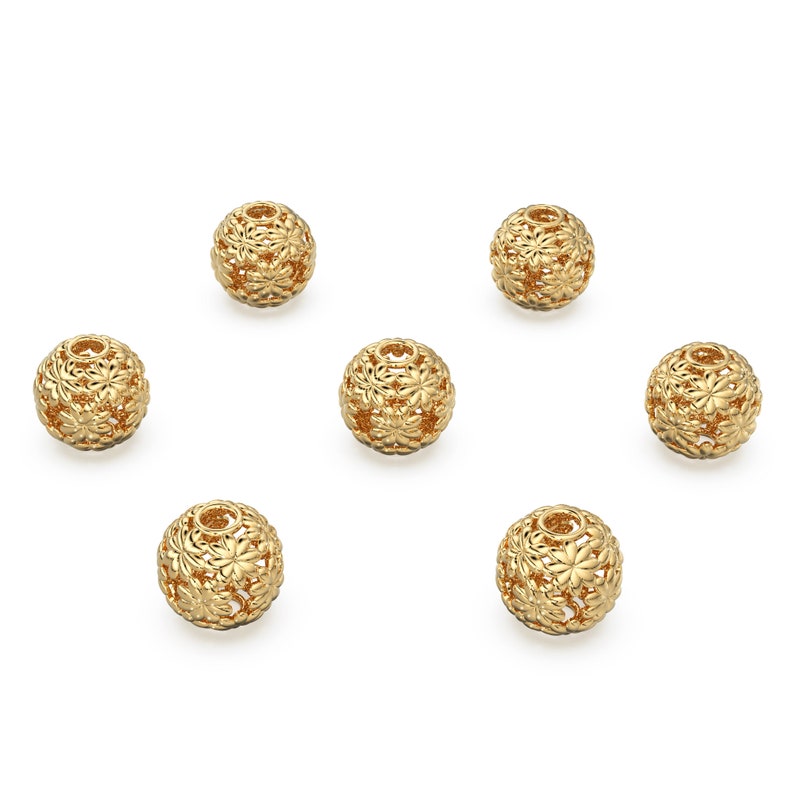 May include: Six gold-colored metal beads with a floral design. The beads are round and have a hollow center.