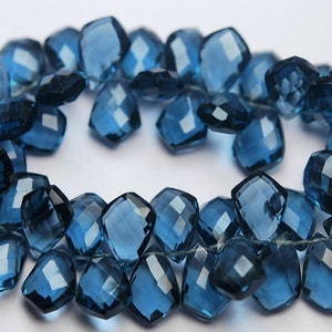 May include: A strand of blue topaz gemstone beads, faceted and cut into a square shape. The beads are strung on a thin thread and have a tassel at the end.