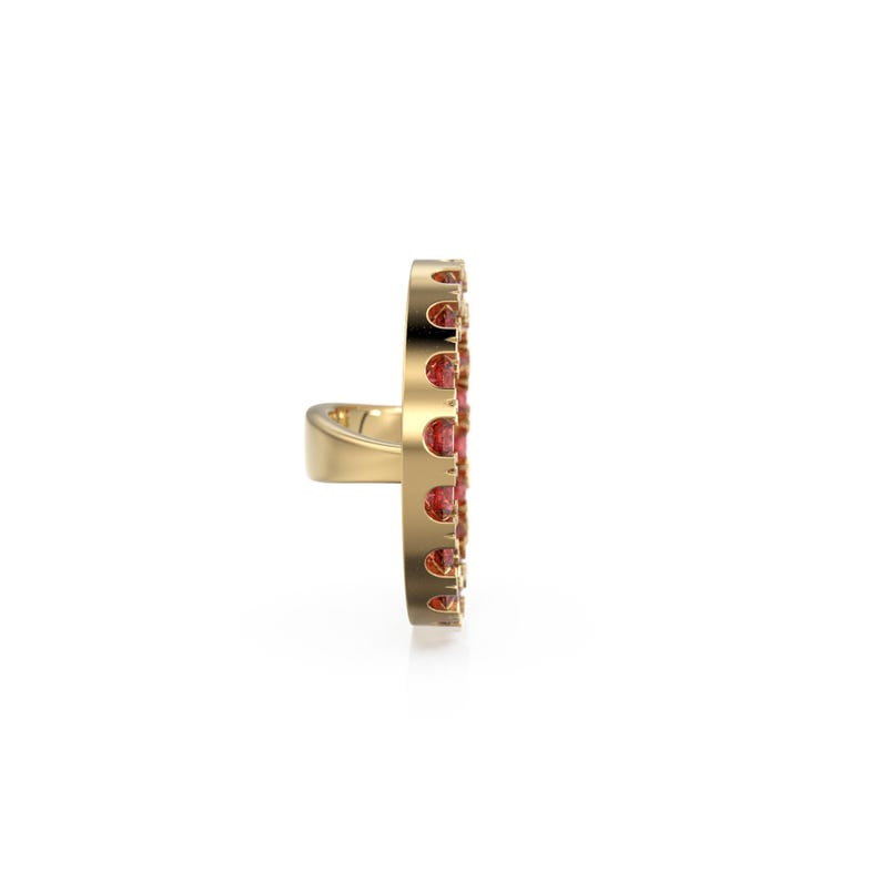 May include: A gold ring with a vertical design, set with small, round, red gemstones. The ring's band is plain, while the gemstone section has a decorative, openwork pattern. The ring is a piece of jewellery.