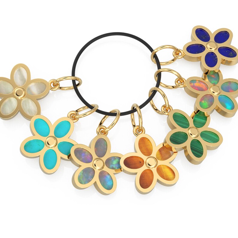 May include: A set of seven gold flower charms with different colored gemstones. The charms are attached to a black elastic band.