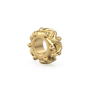May include: A gold-colored metal bead with a textured, wavy design and small, round accents. The bead has a hole in the center for threading.