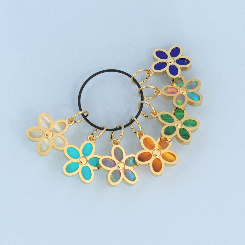 May include: A set of seven gold flower charms with different colored gemstones. The charms are attached to a black ring.