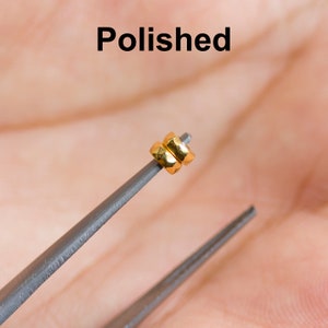 May include: Two gold-colored rings stacked on top of each other, held by a pair of tweezers. The rings are smooth and polished.
