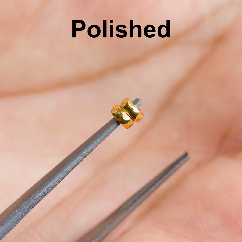 May include: Two gold-colored rings stacked on top of each other, held by a pair of tweezers. The rings are smooth and polished.