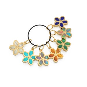 May include: A set of seven gold flower charms with different colored gemstones. The charms are attached to a black elastic cord.
