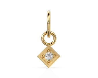Puede incluir: Un colgante de oro con un pequeño diamante en un engaste cuadrado. El colgante tiene un bucle en la parte superior para sujetarlo a una cadena.